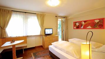 A bedroom with a bed, a desk, a television, and a lamp.