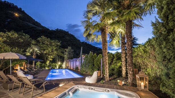 Un bain à remous, des chaises longues et une piscine dans un espace extérieur aménagé, agrémenté d’arbres et offrant une vue sur les montagnes.