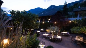 Un espace de restauration en plein air, avec des tables et des chaises, entouré de verdure et offrant une vue sur les montagnes en arrière-plan.