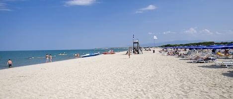 På stranden, solsenger, parasoller og brettseiling