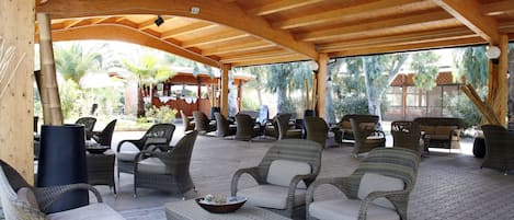 Un patio cubierto al aire libre con mobiliario de mimbre y techo de madera.