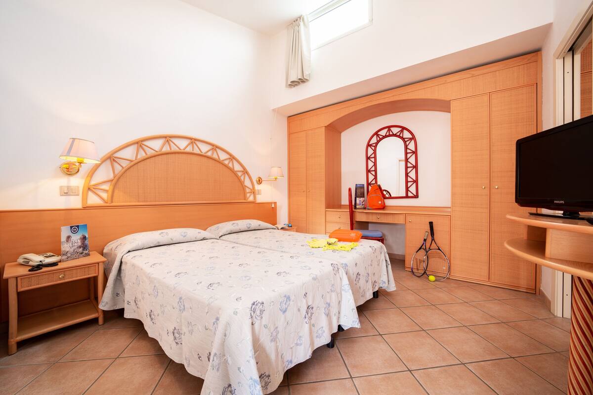 A bedroom with a bed, a TV, a desk, and a mirror.