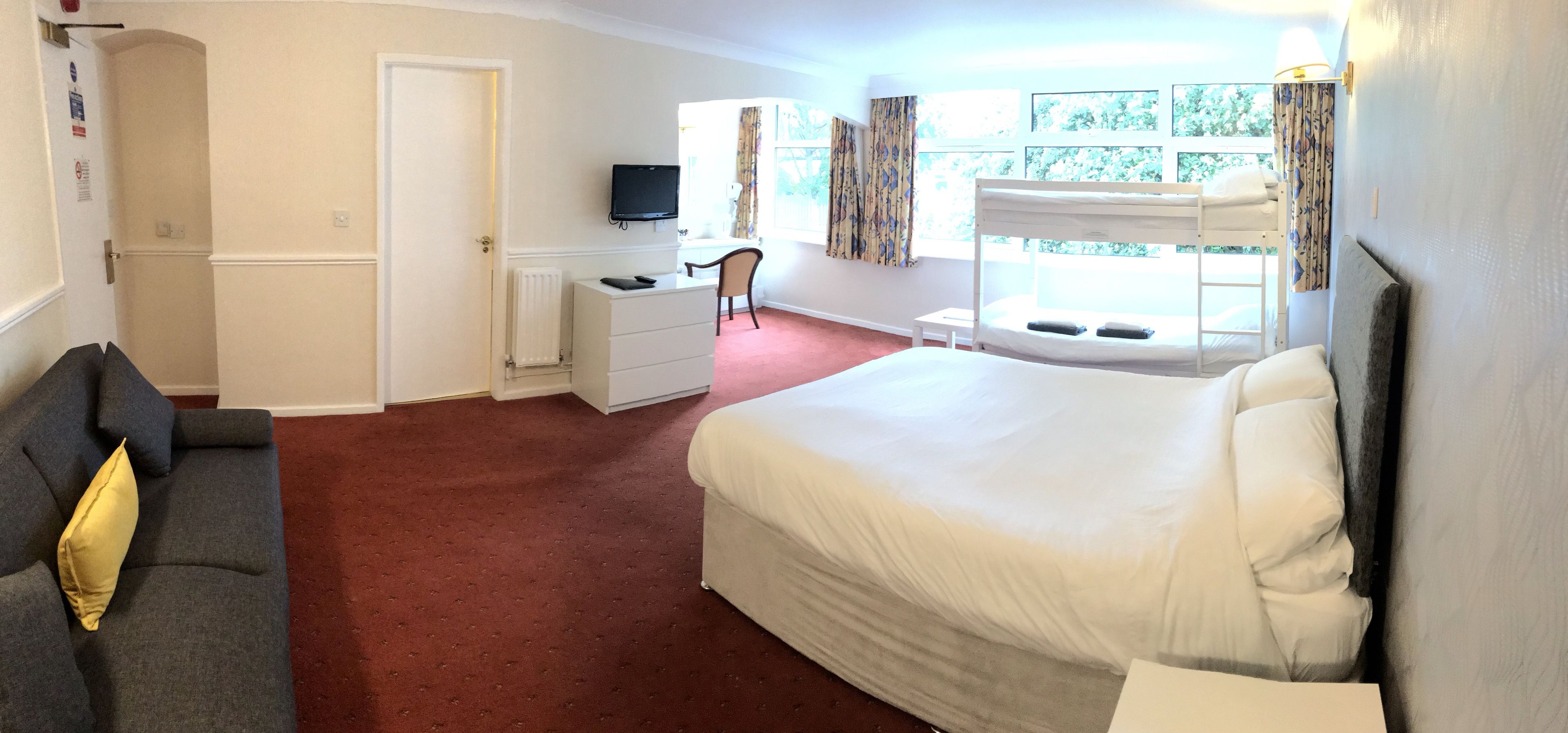 A hotel room with a large bed, a desk with a chair, a television, and a window with curtains.