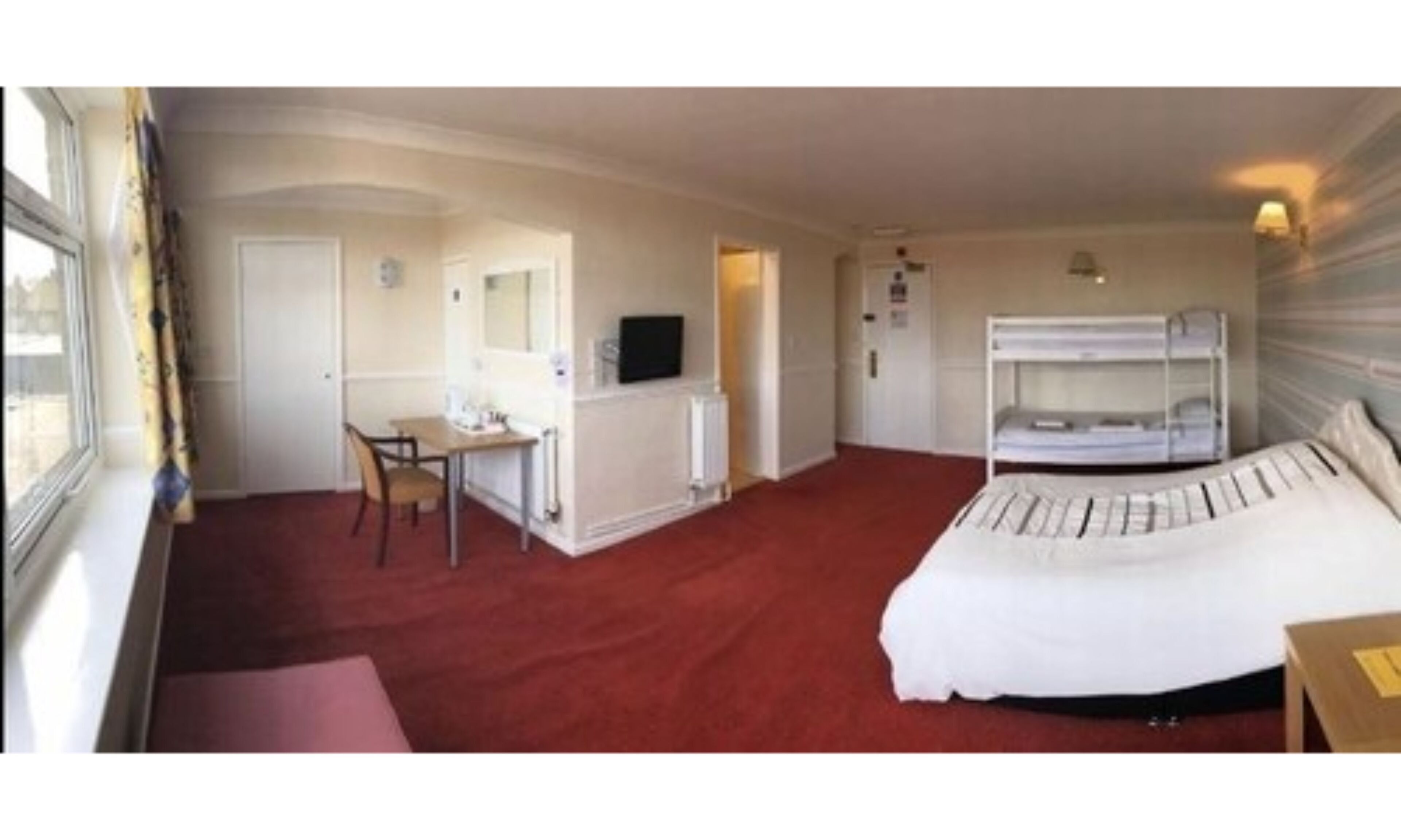 A hotel room with a bunk bed, a desk with a chair, a television, and a window with curtains.