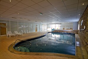 An indoor swimming pool with clear glass walls, lounge chairs, and a tiled floor. - The Highfield (Bradford)
