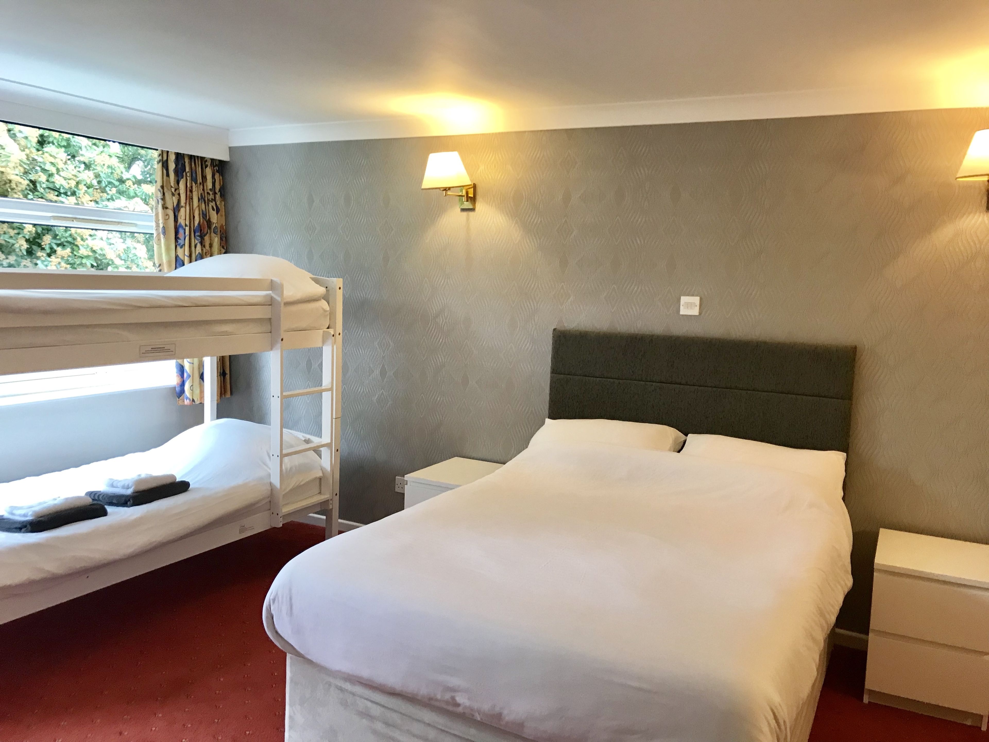 A hotel room with a bunk bed, a single bed, a nightstand, and a lamp.
