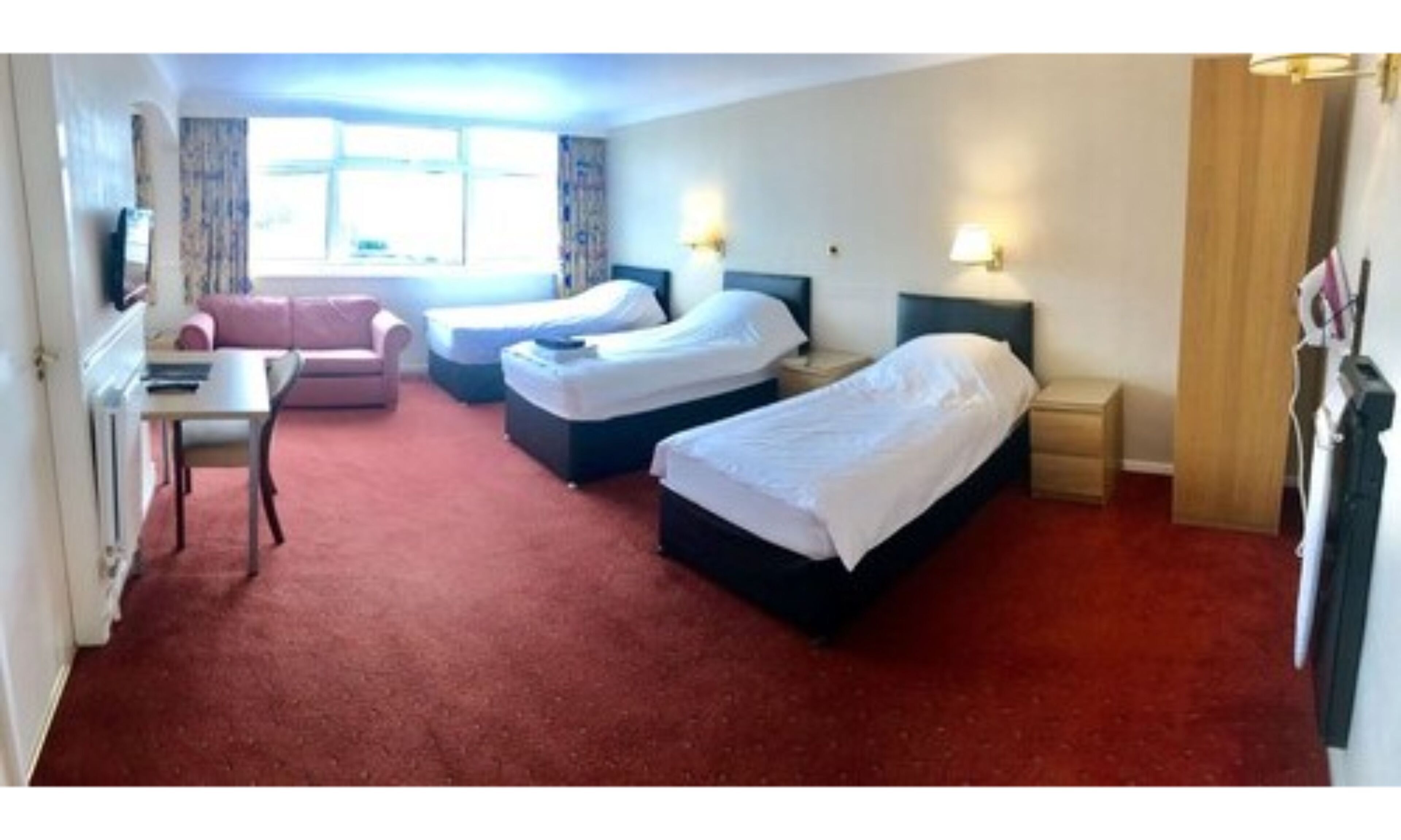 A hotel room with two single beds, a desk, a chair, and a sofa.