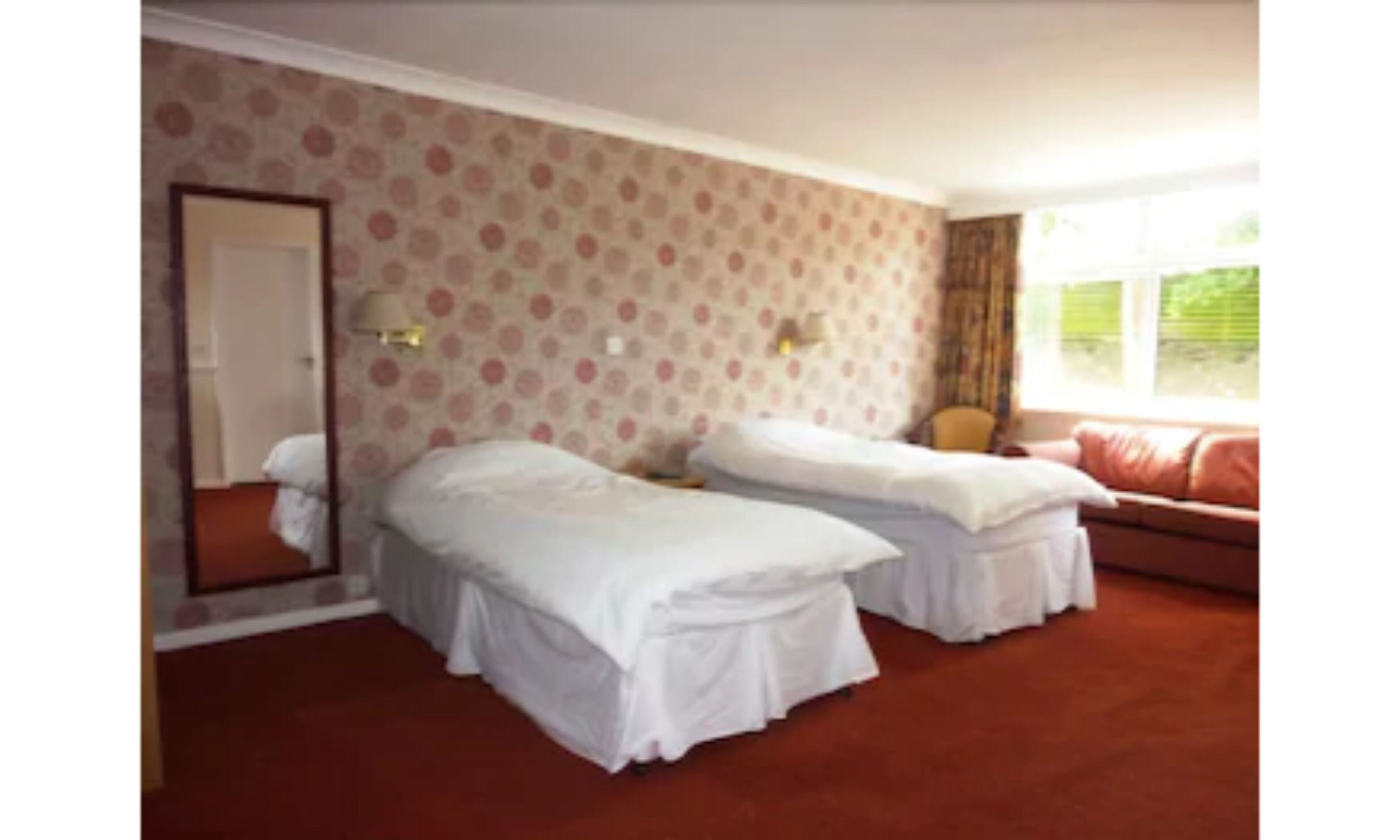A room with two single beds, a sofa, a mirror, and a window with curtains.