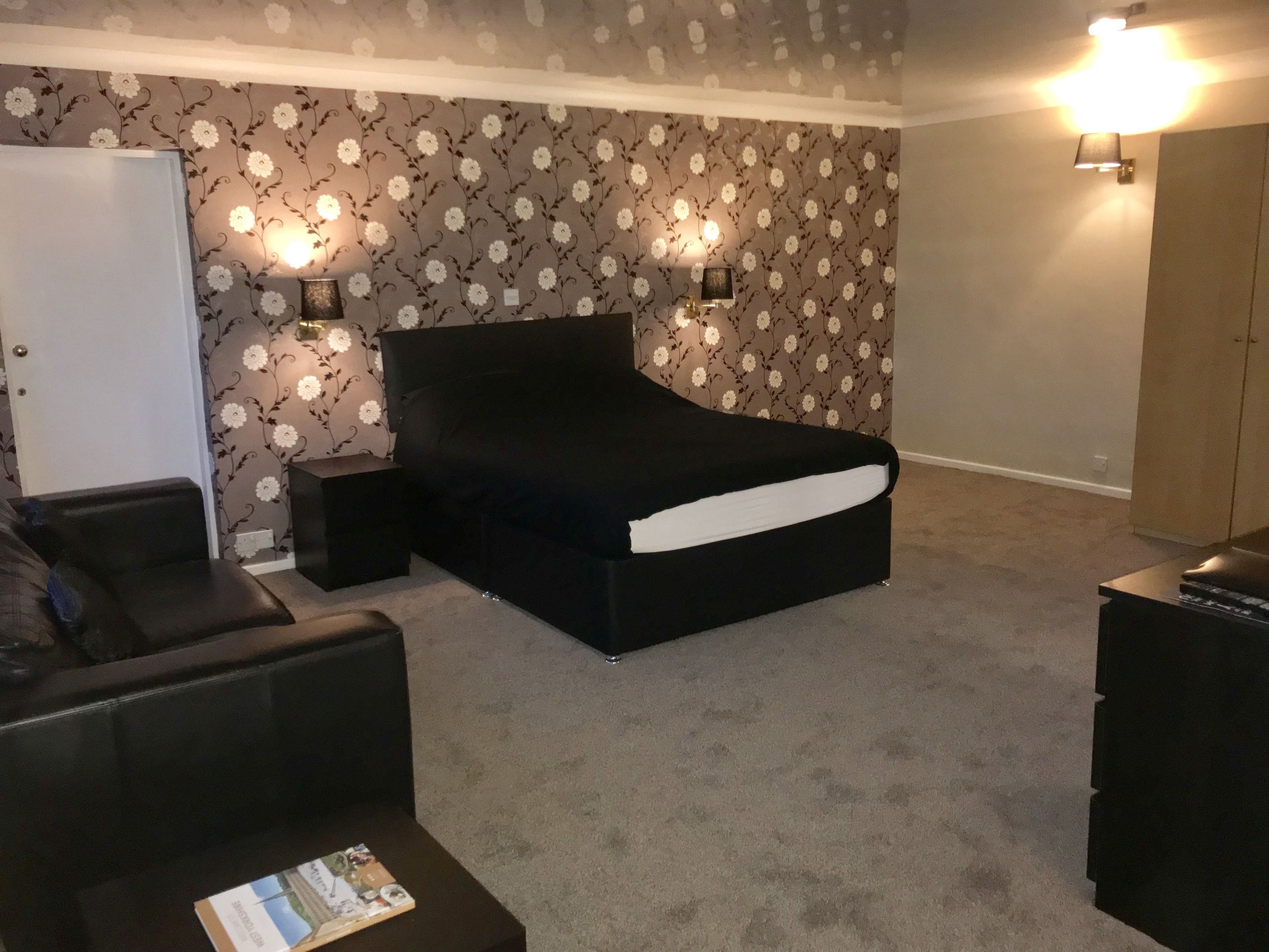 A bedroom with a black bed, two bedside lamps, a white wardrobe, and a black leather chair.