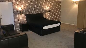 A bedroom with a black bed, two bedside lamps, a white wardrobe, and a black leather chair.