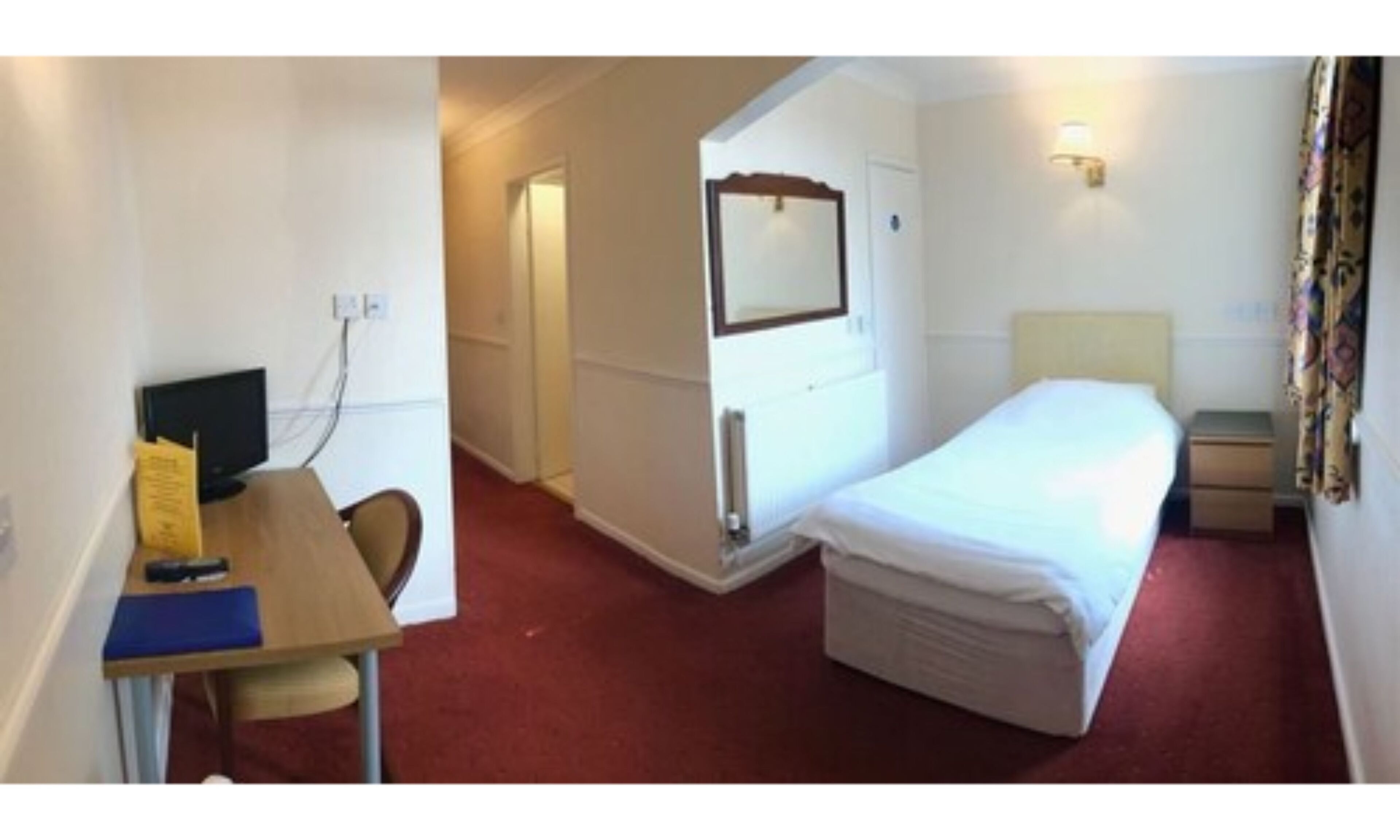 A hotel room with a bed, a desk with a chair, a television, and a mirror.