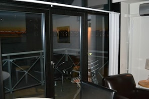 A room with a glass door leading to an outdoor area with chairs and a table.
