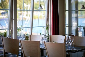 A dining area with tables set for four, large windows, and hanging pendant lights.