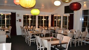 A restaurant with multiple tables and chairs, large windows, and hanging lanterns. - Park Hotel Motala (Motala)
