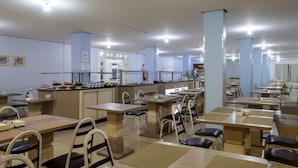 A spacious dining area with multiple tables and chairs, a kitchen area in the background, and light blue walls. - Hotel Seibt (Foz do Iguaçu)