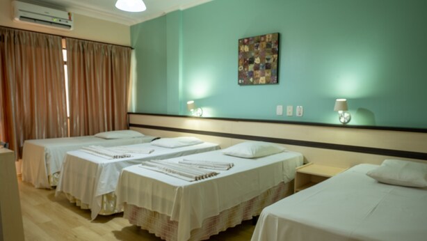 A hotel room with three beds, a wooden floor, a teal wall, and a quilted artwork. - Hotel Seibt (Foz do Iguaçu)