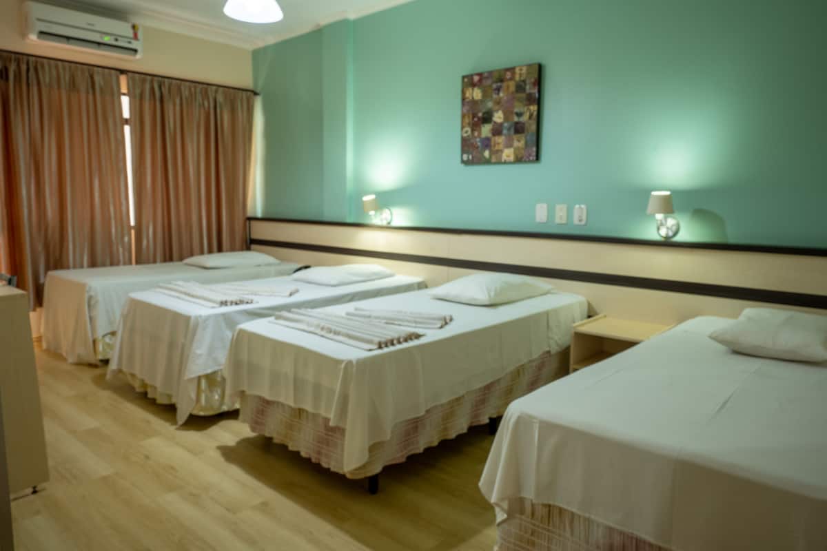 Habitación de hotel con tres camas, piso de madera, pared verde azulado y una obra de arte acolchada.