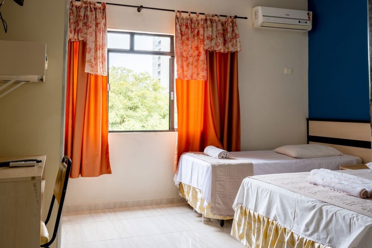 Una habitación con dos camas, televisión, aire acondicionado y ventana con cortinas.