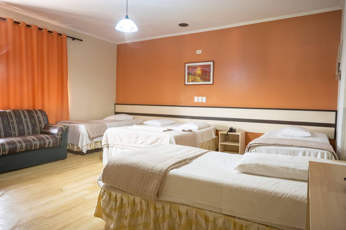 Habitación de hotel con dos camas individuales, un sofá, una mesita y un cuadro en la pared.