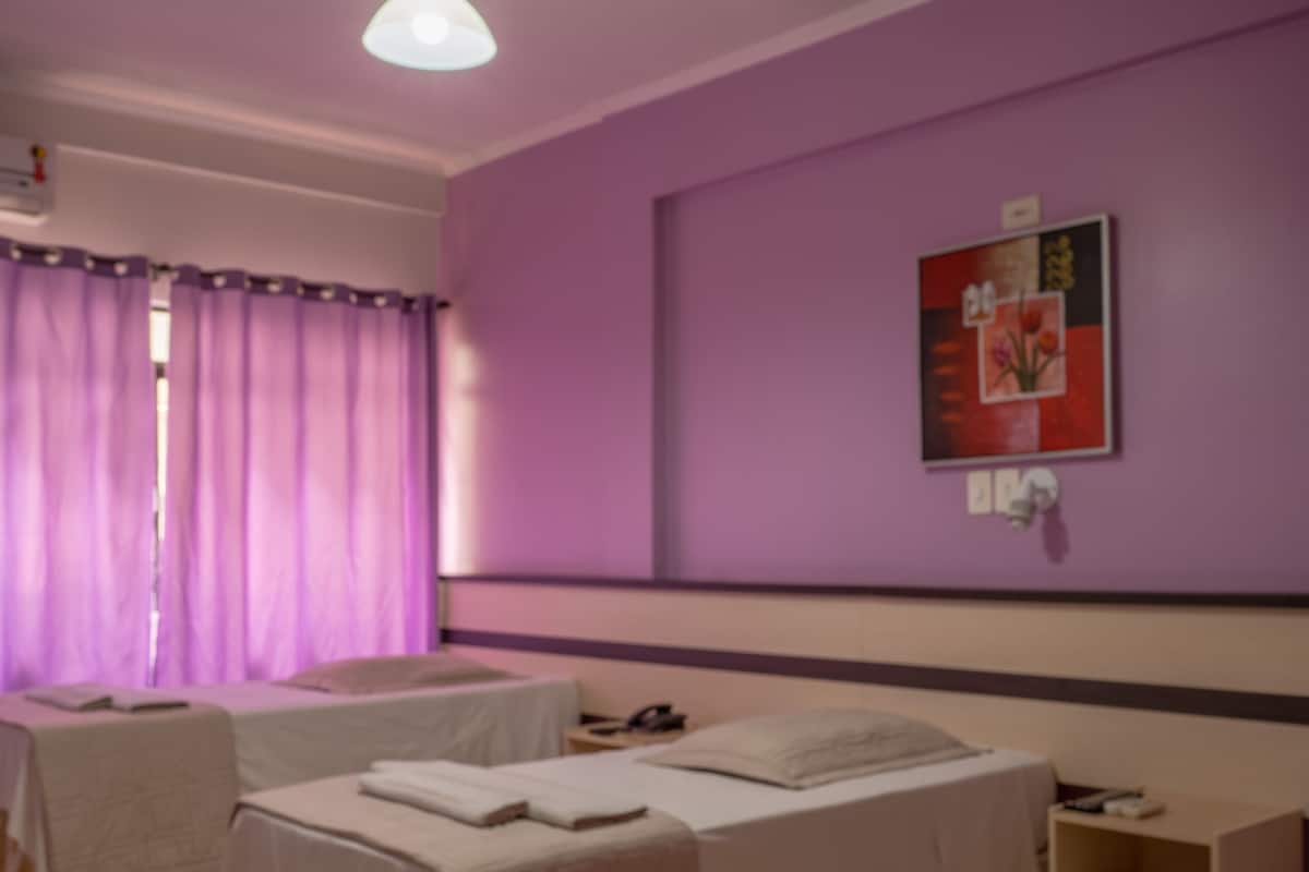 Una habitación con dos camas, suelo de madera y una pared morada.
