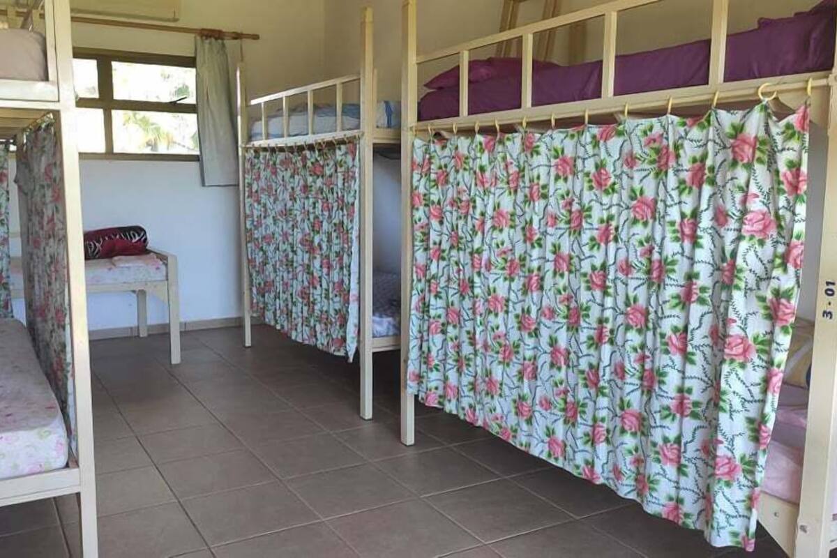 A dormitory room with bunk beds, floral curtains, and a small table with a chair.