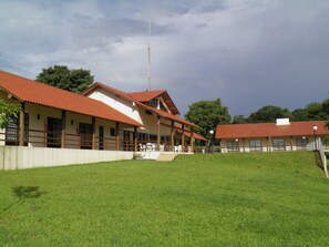 A building with a red-tiled roof, a covered patio area, and a grassy lawn. - Ipelandia Park Golf Hostel (Foz do Iguaçu)