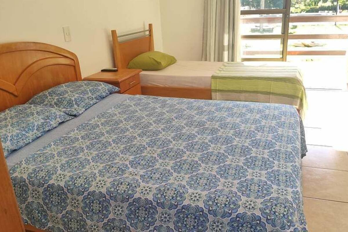 A bedroom with a large bed, a nightstand, a green pillow, and a window with curtains.