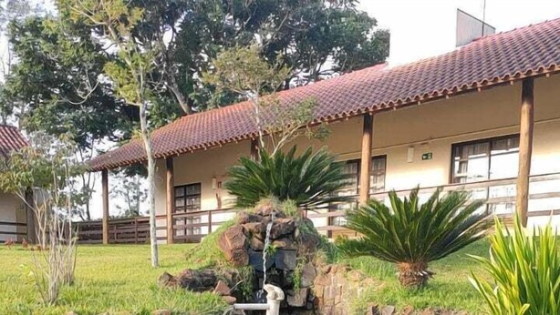 Un estanque con cascada y rocas, rodeado de hierba y plantas, con un edificio al fondo.