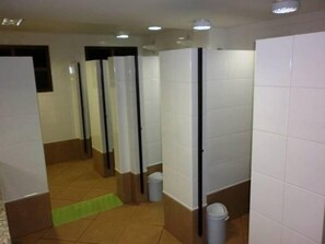 A public restroom with multiple stalls, a trash bin, and a green mat on the floor. - Ipelandia Park Golf Hostel (Foz do Iguaçu)