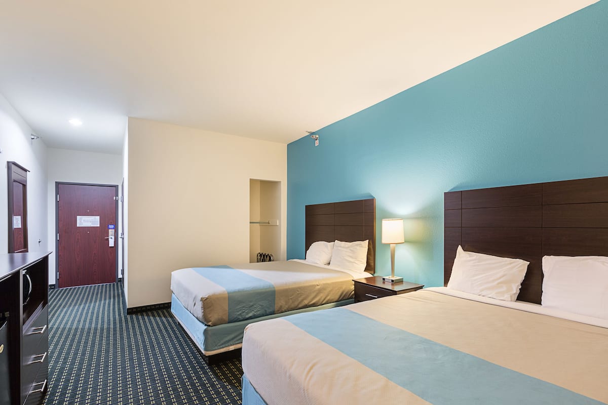 A hotel room with two beds, a desk, a lamp, and a wardrobe.