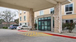 L’entrée d’un hôtel, avec une allée couverte, des piliers en pierre et une porte d’entrée en verre.