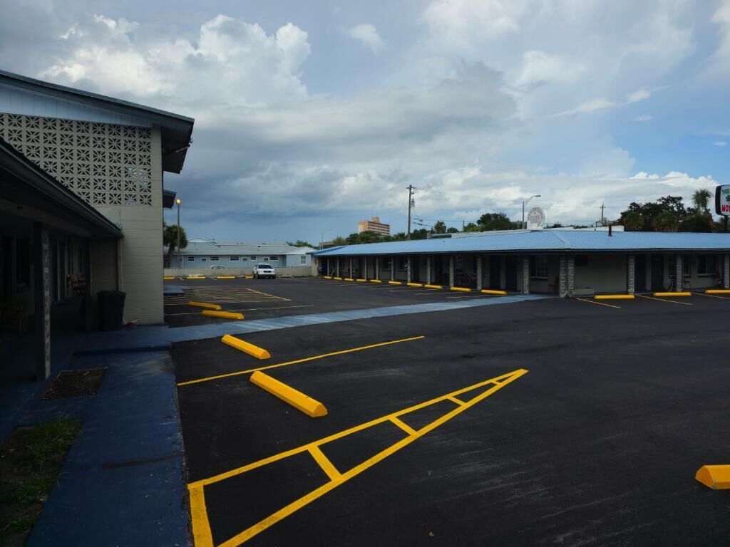 Un parking avec des places délimitées et, au fond, un bâtiment surmonté d’un toit bleu.