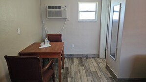A room with a wooden dining table, two chairs, an air conditioning unit, a window, and a door. - Three Oaks Motel (Titusville)