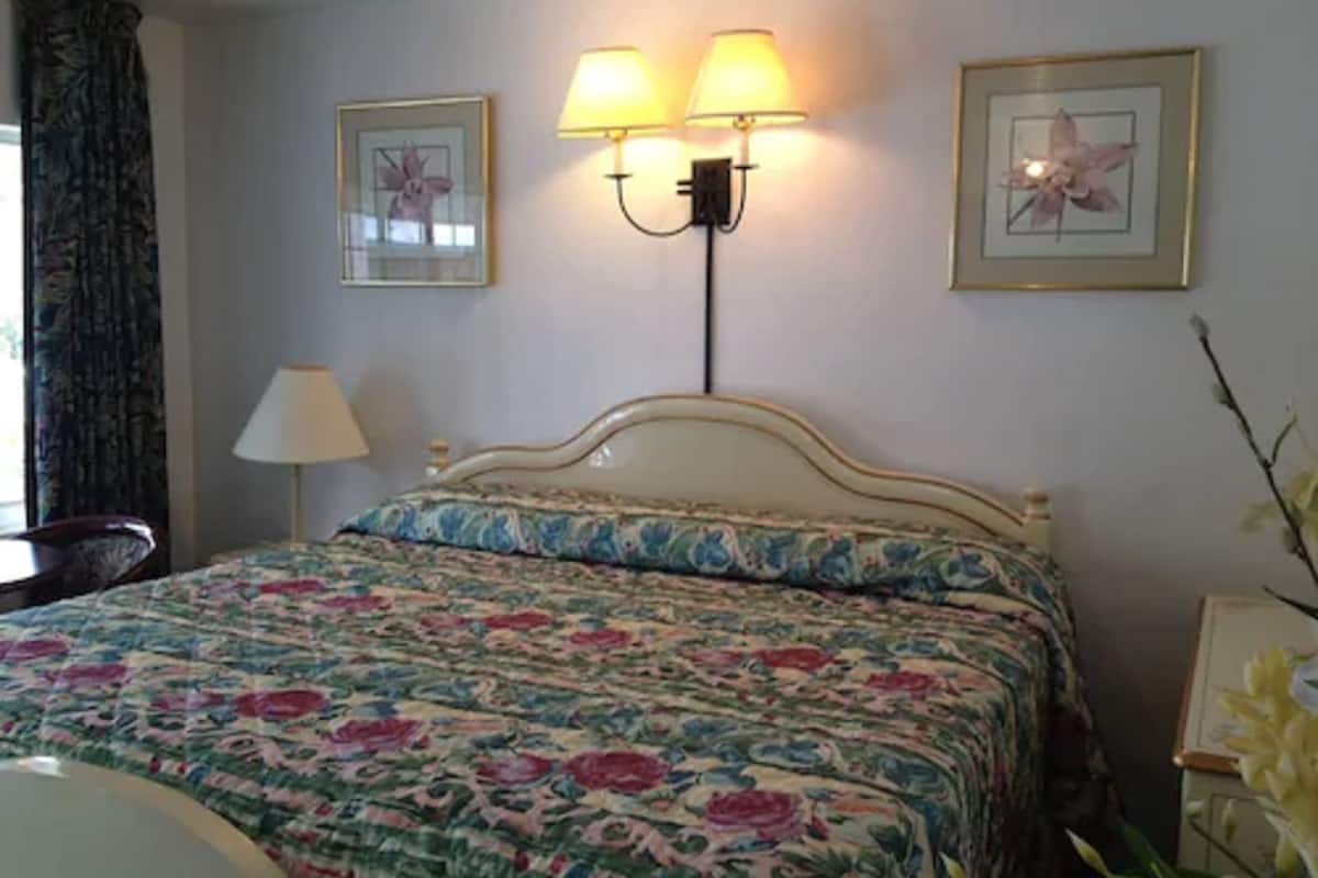 A neatly made bed with floral bedding, two wall-mounted lamps, and framed pictures on the wall.