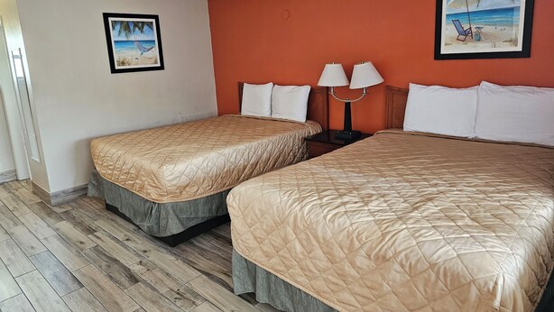 A hotel room with two beds, a wooden floor, and two wall-mounted lamps. - Three Oaks Motel (Titusville)