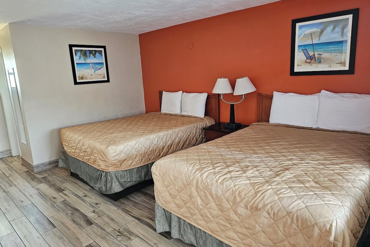 A hotel room with two beds, a wooden floor, and two wall-mounted lamps.