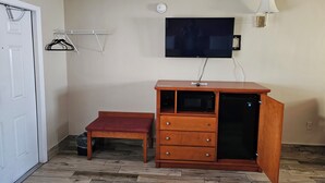 A room with a wooden bench, a TV mounted on the wall, a wooden cabinet with drawers, and a coat rack. - Three Oaks Motel (Titusville)
