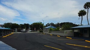 A parking lot with marked spaces and a building with a blue roof in the background. - Three Oaks Motel (Titusville)
