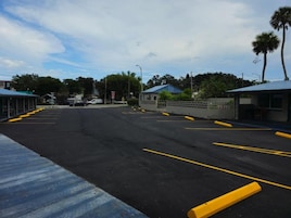 Um parque de estacionamento com espaços demarcados e um edifício com telhado azul ao fundo.