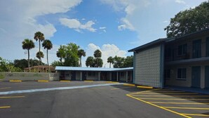 A parking lot with marked spaces, a building with a patterned facade, and palm trees in the background. - Three Oaks Motel (Titusville)