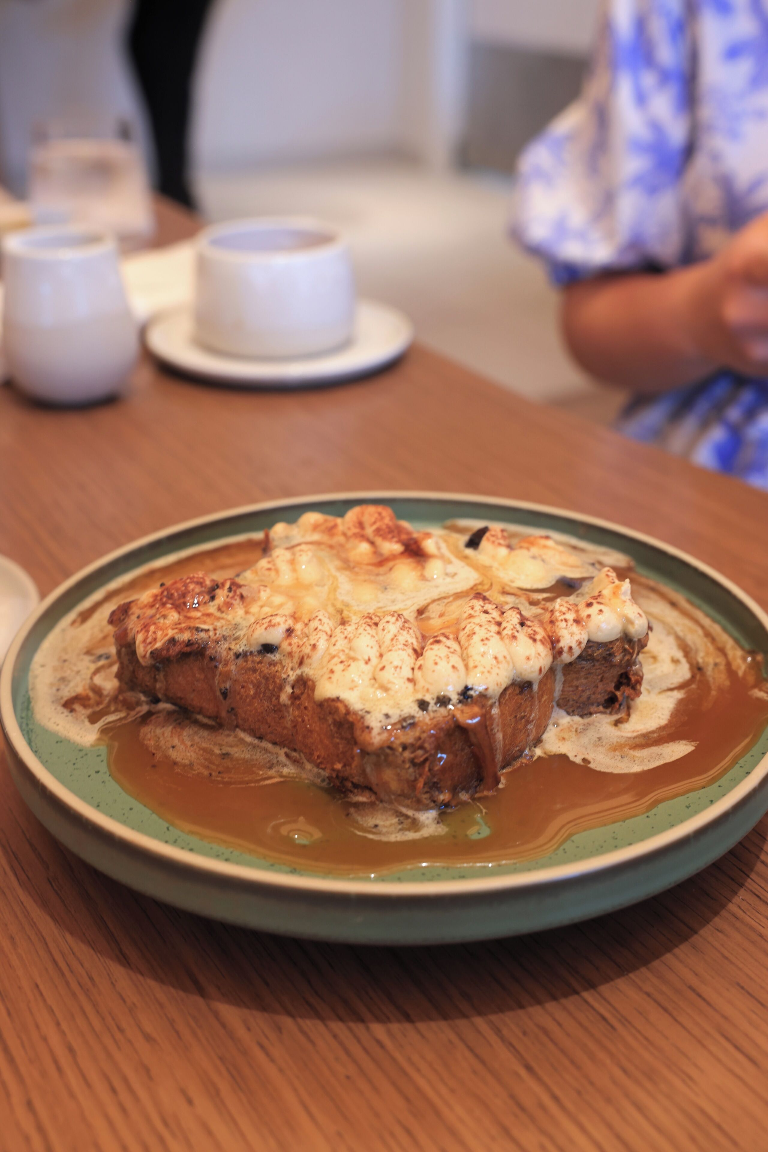 A plate of food with a creamy topping, a wooden table, and a cup in the background.