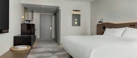 Una habitación de hotel moderna con una cama grande, un televisor de pantalla plana, un escritorio con una lámpara y una puerta que da a otra habitación.