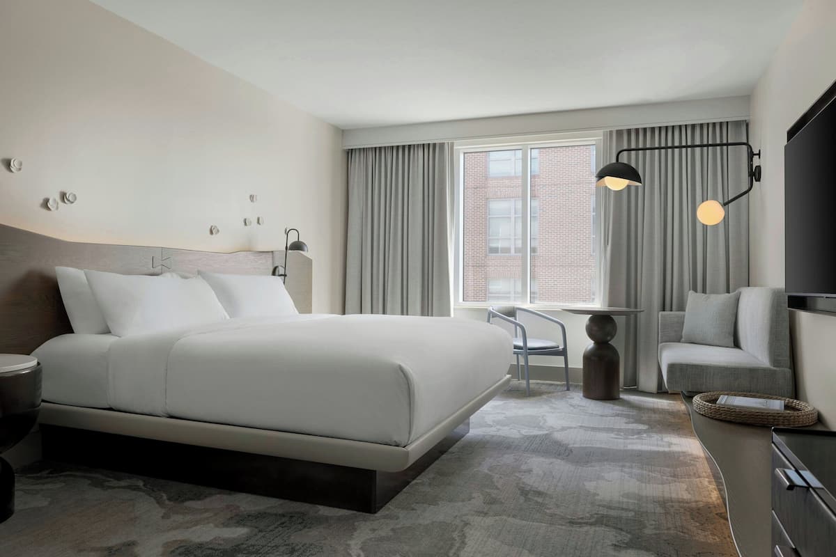 Una habitación de hotel moderna con una cama grande, un escritorio, una silla, un televisor y una ventana con cortinas.