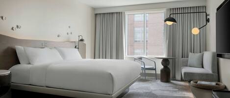 Una habitación de hotel moderna con una cama grande, un escritorio, una silla, un televisor y una ventana con cortinas.