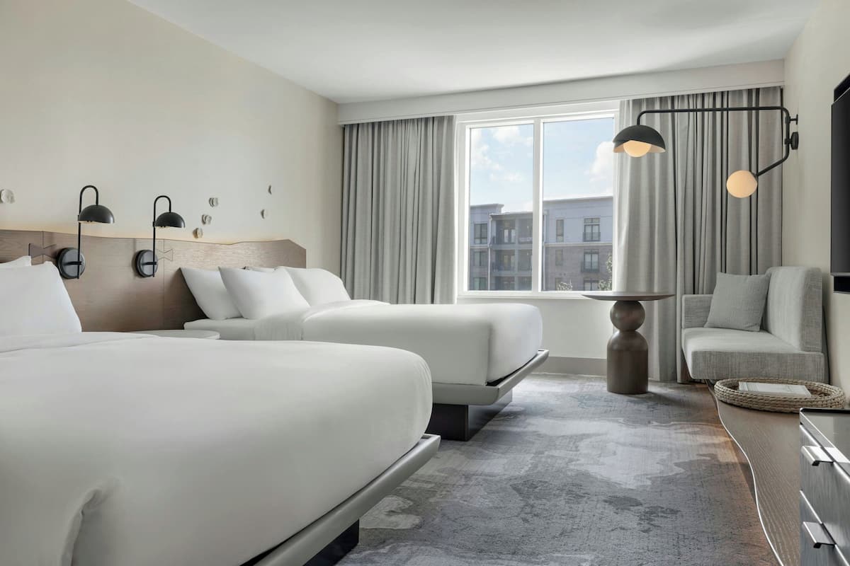 Habitación de hotel con dos camas, un sofá, una lámpara y vistas a edificios.