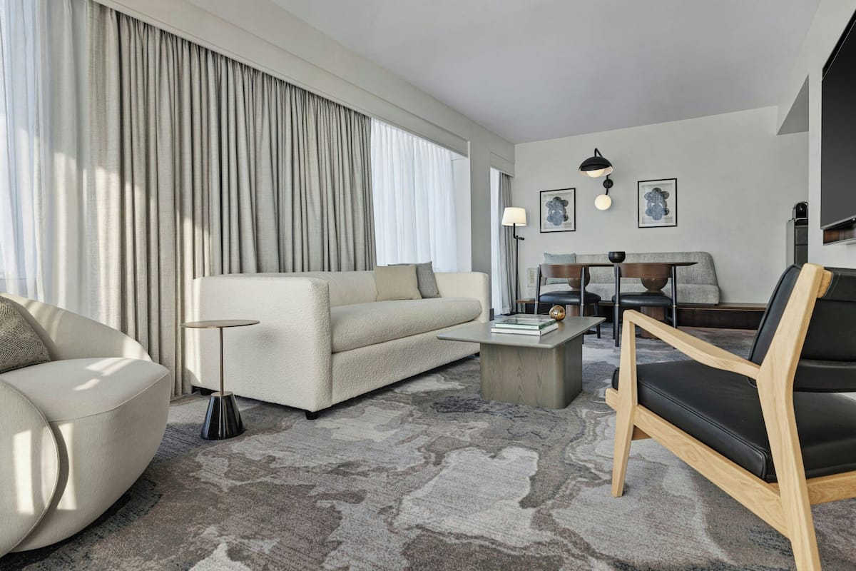 Una habitación de hotel moderna con sofá, sillón, mesa de centro y televisión.