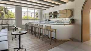 A modern bar area with a long counter, bar stools, and a seating area with a sofa and tables.