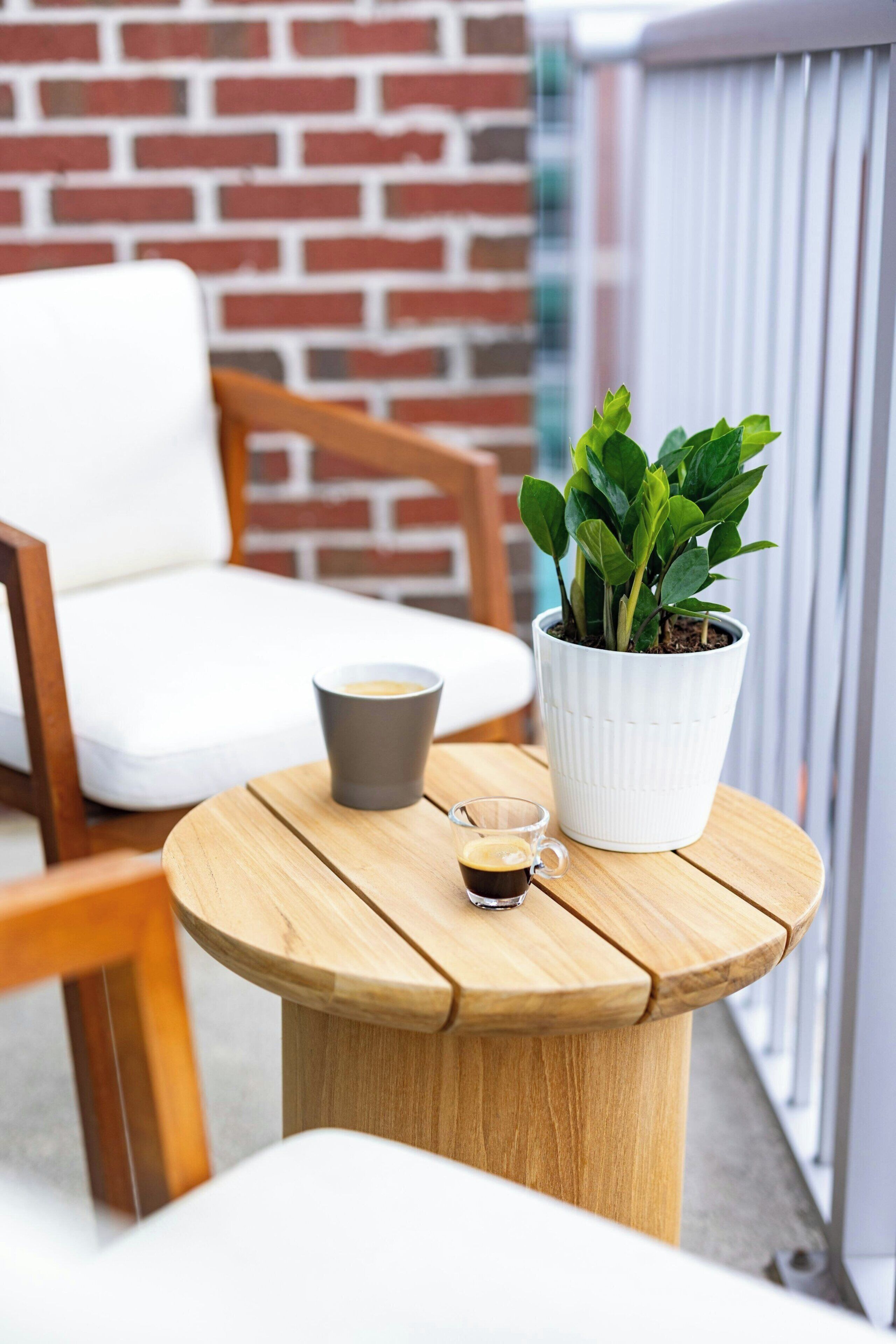 A round wooden table with a potted plant, a cup of coffee, and a glass of coffee.