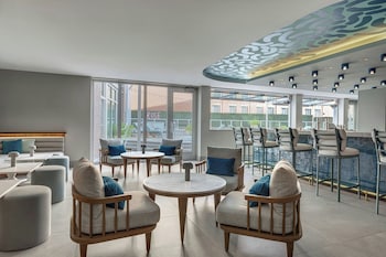 A modern bar area with a long counter, bar stools, and a seating area with a sofa and tables. at Live Oak, Charleston Historic District, a Tribute Portfolio Hotel