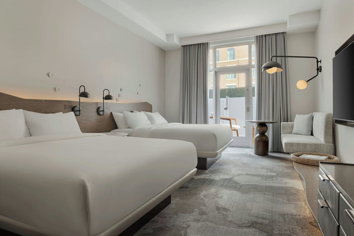 Una habitación de hotel moderna con dos camas, un sofá, un televisor y un amplio ventanal con cortinas.